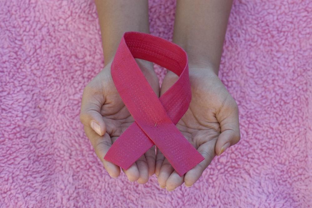 A person holding a pink ribbon for breast cancer awareness