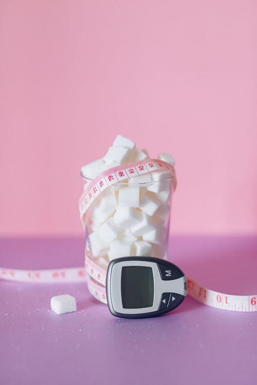 A glass of sugar cubes with a measuring tape and glucometer