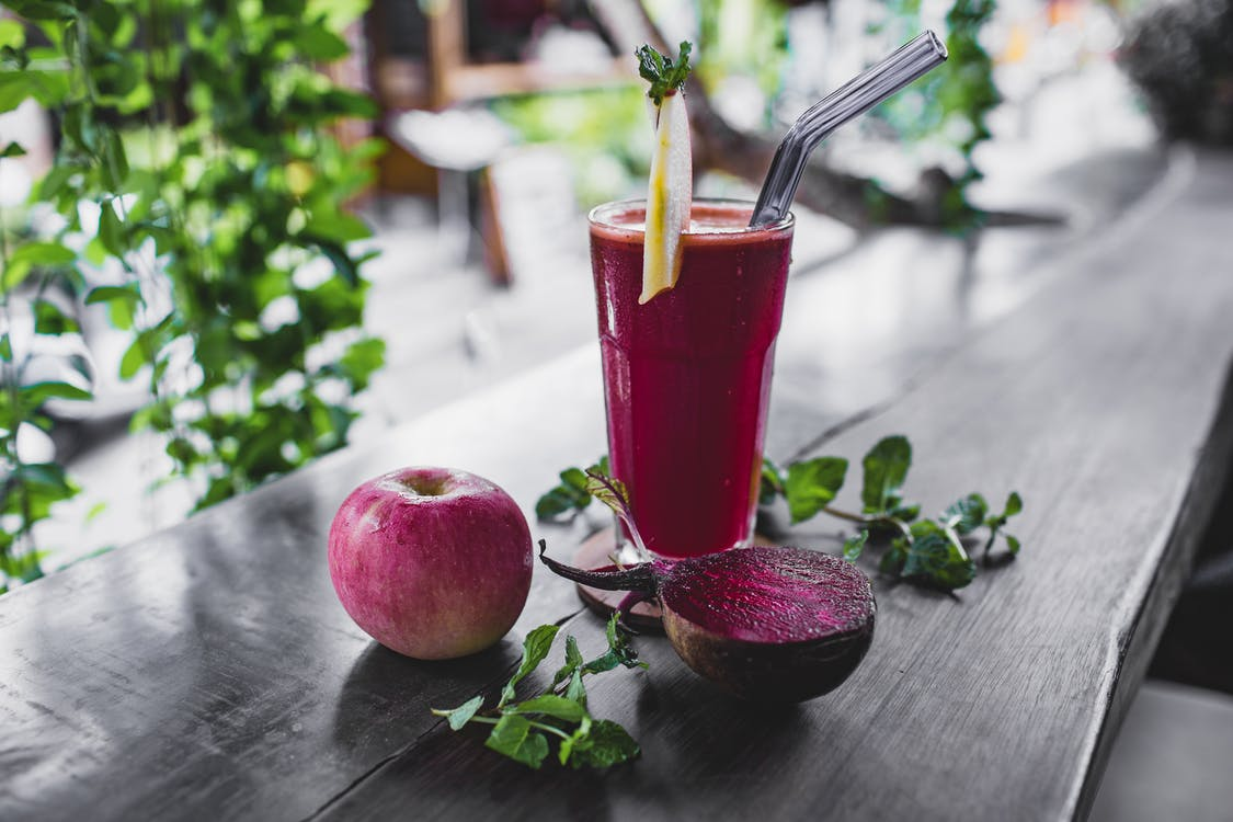 A glass with a red drink and an apple and half-cut beetroot lying next to it